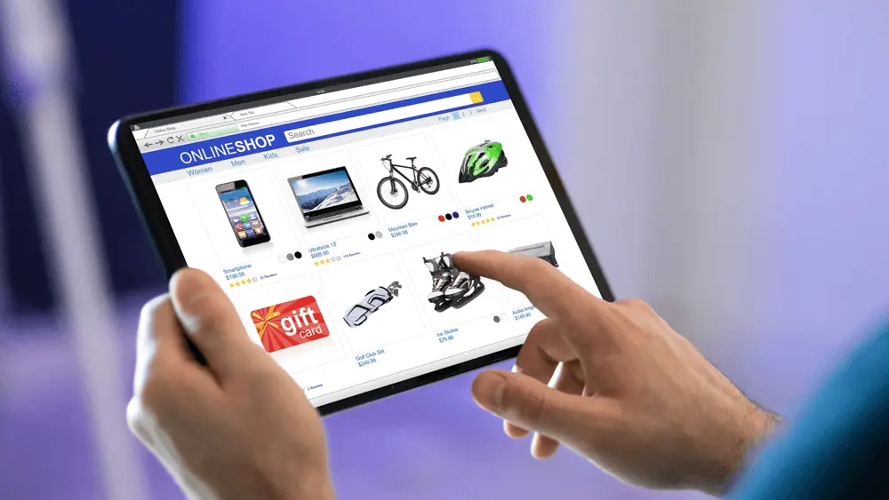Person browsing an online shopping website on a tablet, showing product listings like a smartphone, bicycle, helmet, and gift card.
